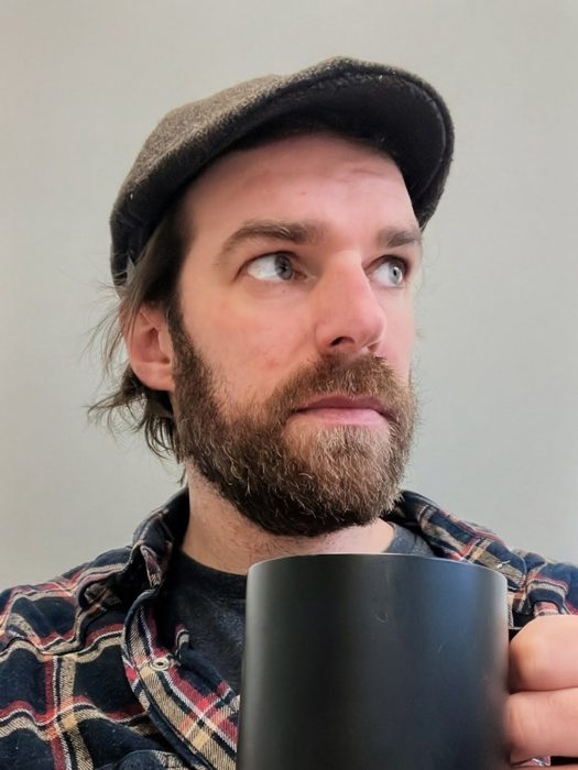 Ashley Keeler in a flat cap holding a black mug