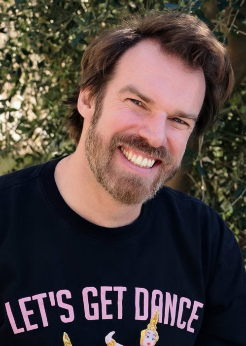 Ashley Keeler laughing, head tilted, in front of an olive tree