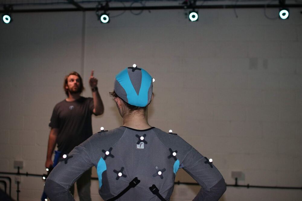Ashley in a grey t-shirt watching a trainee in a motion capture suit and helmet