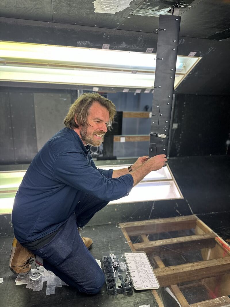 Ashley kneeling beside a wind tunnel test section, fixing tracking markers to a wing model